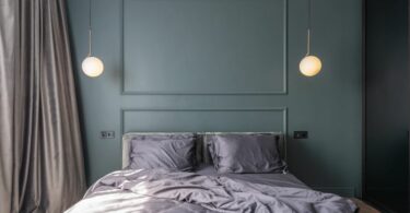 Interior design of modern bedroom with unmade bed under luminous lamps at sunlight