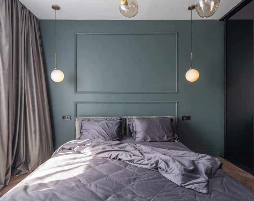 Interior design of modern bedroom with unmade bed under luminous lamps at sunlight